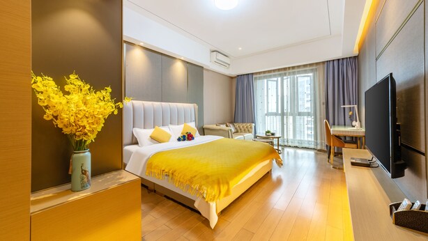 A modern hotel room with a large bed, a desk, a TV, and a view of the city. - Manhattan Langde Apartment (Guangzhou)