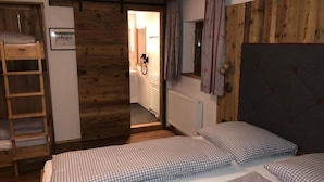 Una habitación con dos camas, un armario de madera, un radiador y un baño visible a través de una puerta abierta.