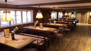 Un restaurante acogedor con mesas y bancos de madera, iluminación cálida y ventanas amplias.