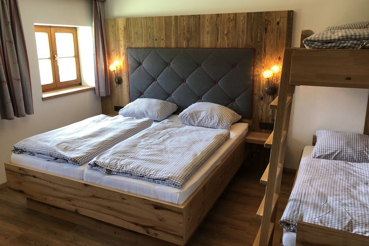 Una cama de madera con cabecera capitonada, dos mesitas de noche con lámparas y un ventanal con cortinas.