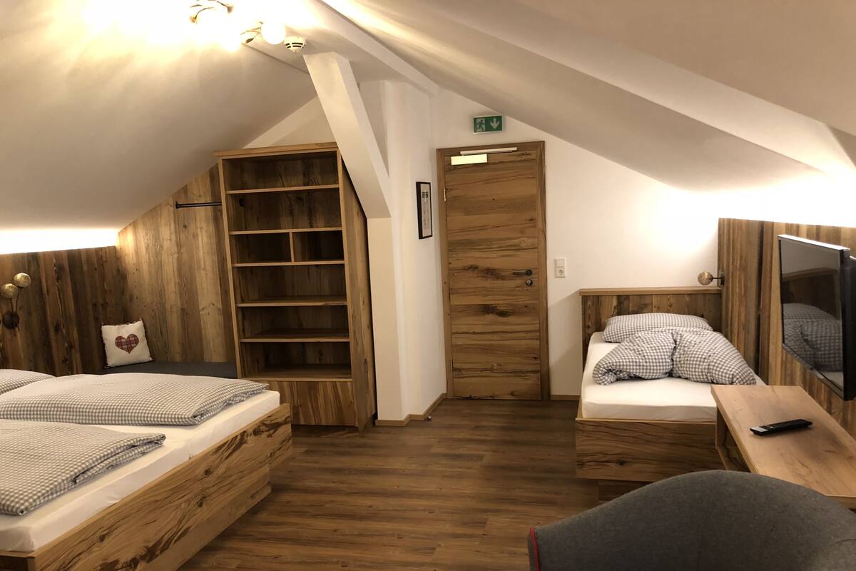 Un dormitorio acogedor en el ático con dos camas de madera, una estantería empotrada y un televisor montado en la pared.