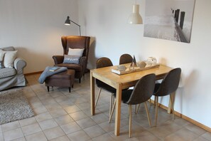 Un comedor con una mesa y sillas de madera, un sillón de cuero marrón, una lámpara y un cuadro en la pared.