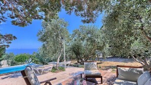 An outdoor seating area with a pool, lounge chairs, and a wooden table with a bottle and glasses.