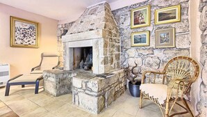 A stone fireplace with a fire, a chair, and framed pictures on the wall.