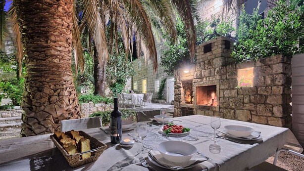An outdoor dining area with stone walls, a fire pit, and a table set for two with bread and wine.