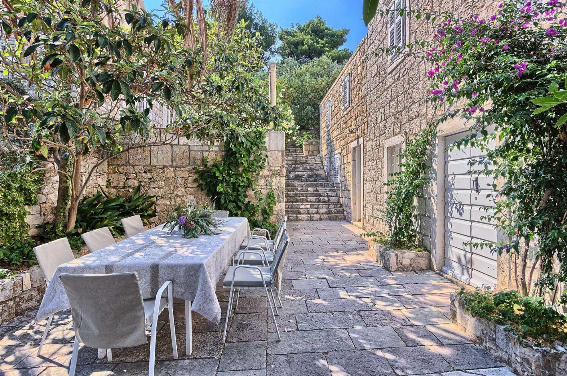 A stone courtyard with a table set for dining, surrounded by greenery and a stone building.
