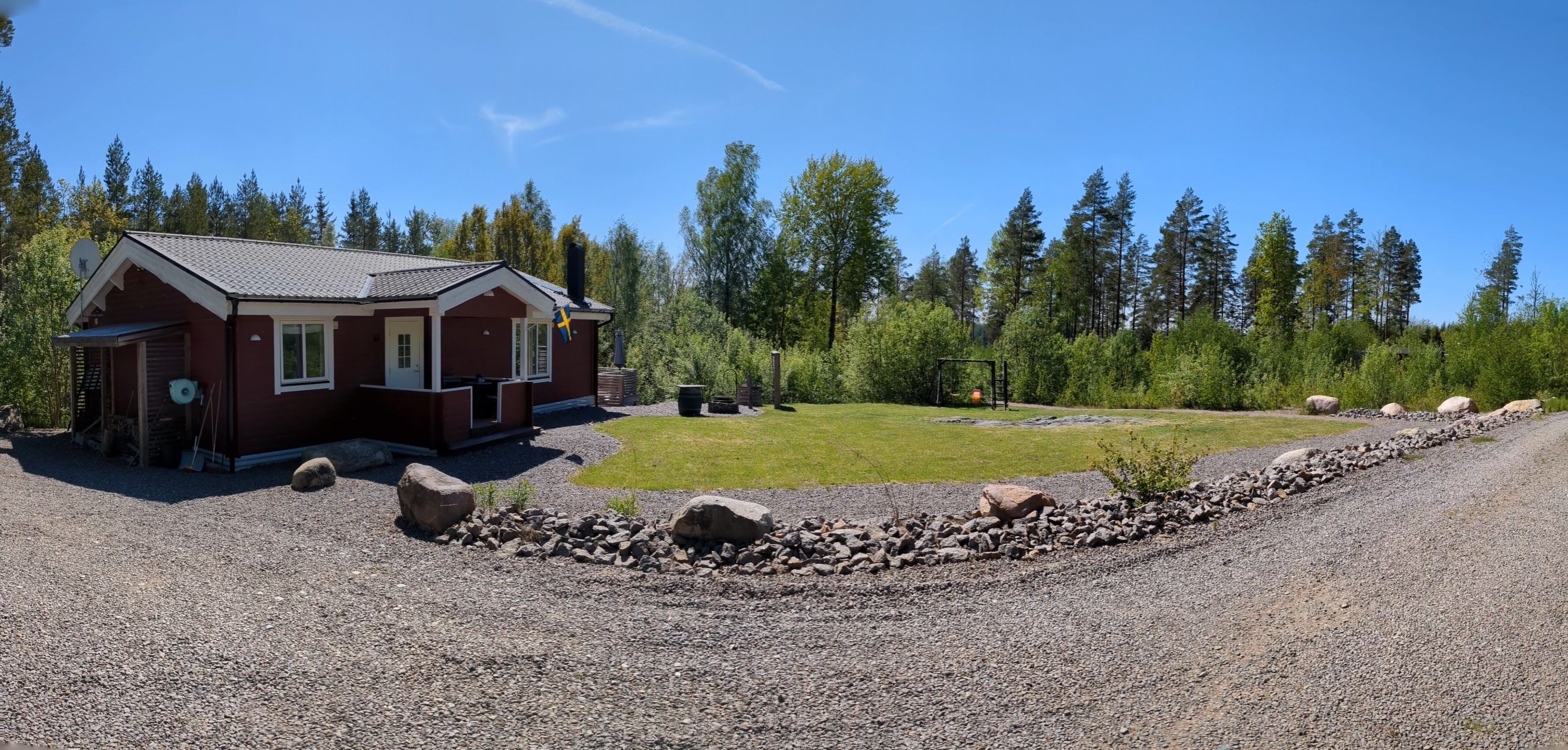 Une cabane avec une allée en gravier, une pelouse et une forêt en arrière-plan.