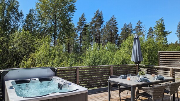 Une terrasse en bois avec un jacuzzi, une table dressée pour le repas et un parasol.