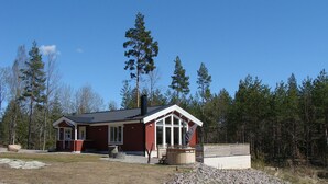 Une cabane rouge dotée d’une grande fenêtre et d’une cheminée, entourée d’une forêt.