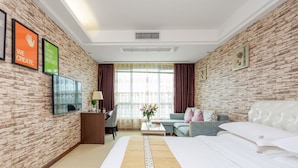 Hotelkamer met een bakstenen muur, een bed met wit beddengoed, een bank, een bureau met stoel en een groot raam met gordijnen.