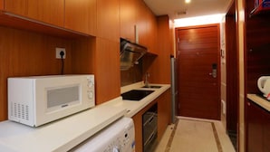 Een kleine keuken met houten kastjes, een magnetron, een spoelbak en een koelkast.