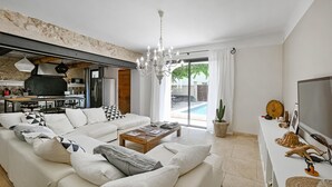 A modern living room with a large sofa, a coffee table, and a TV on a white console. There is a kitchen area with a stove and refrigerator visible. - Luxurious home in Vedène (Vedène)