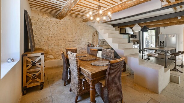 A rustic dining area with a stone wall, wooden furniture, and a staircase leading to a kitchen. - Luxurious home in Vedène (Vedène)