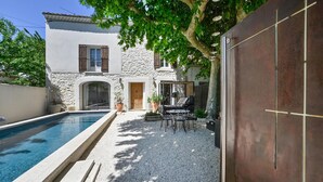 A poolside area with a stone wall, a wooden door, and a covered seating area with chairs and a table. - Luxurious home in Vedène (Vedène)