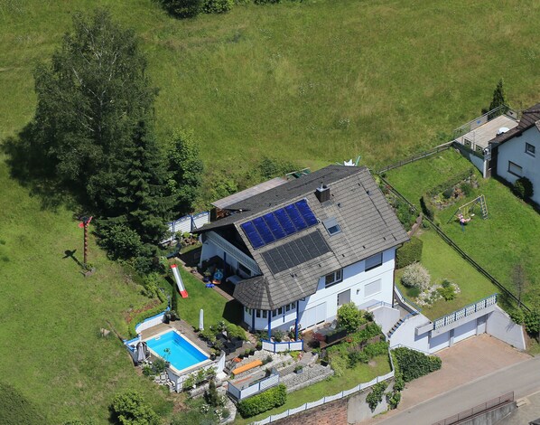 Vista aérea de una casa con piscina, paneles solares y patio cercado.