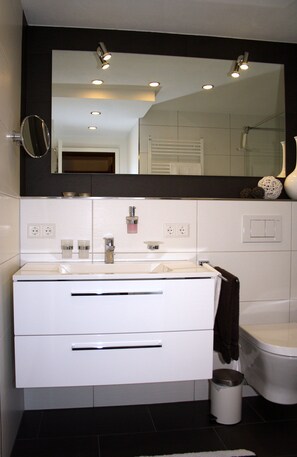 Un baño moderno con tocador blanco, un espejo grande y un inodoro.