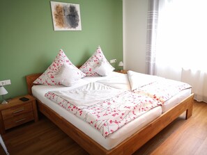 Una cama bien hecha con ropa de cama floral, una mesita de noche con una lámpara y un enchufe en la pared.