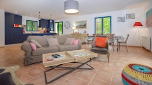 A modern living room with a sofa, coffee table, and chairs. There is a kitchen area with cabinets and a dining table. - Stunning home in Nessa (Nessa)
