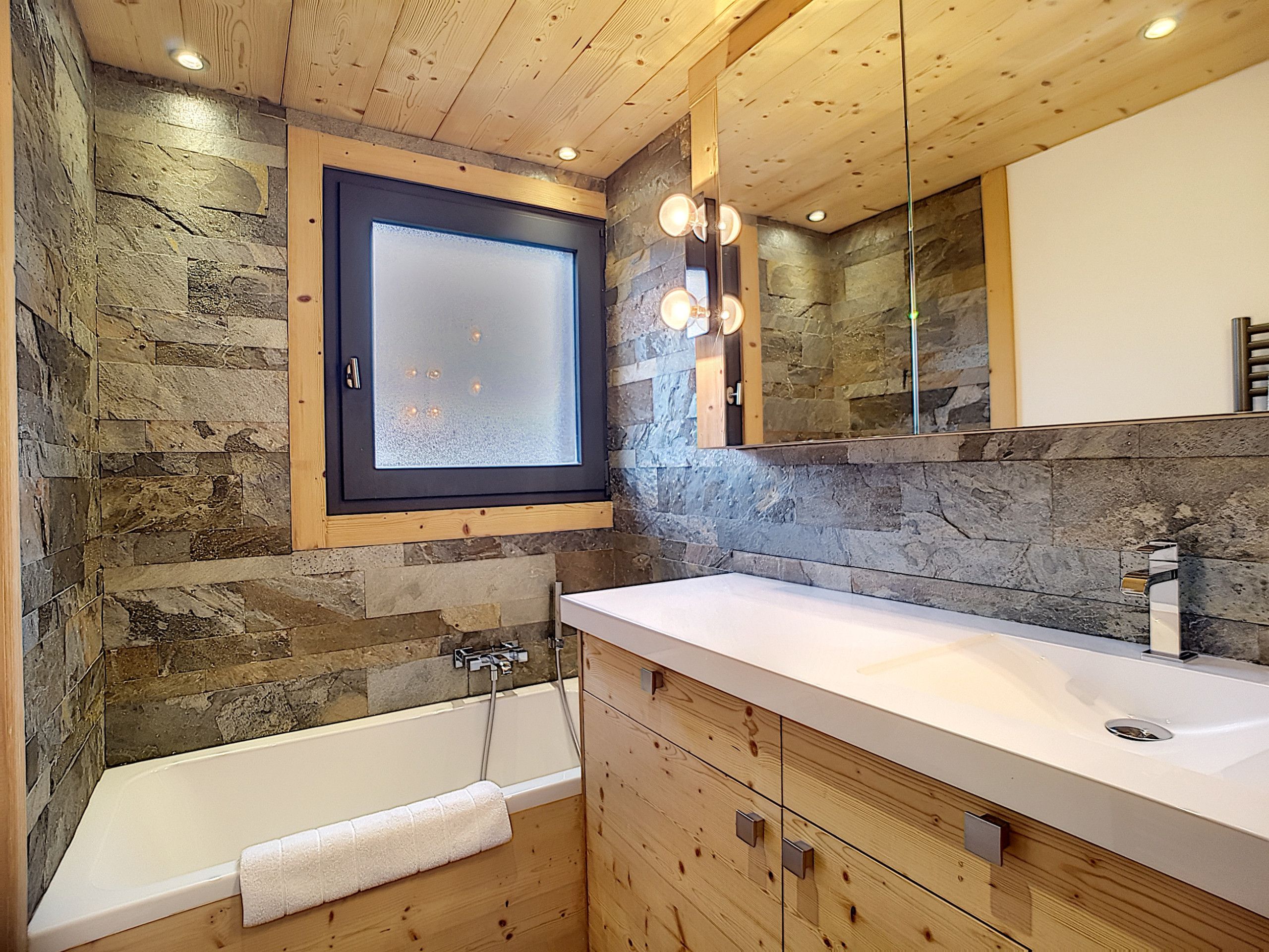 A bathroom with a stone wall, wooden ceiling, a large mirror, and a bathtub.