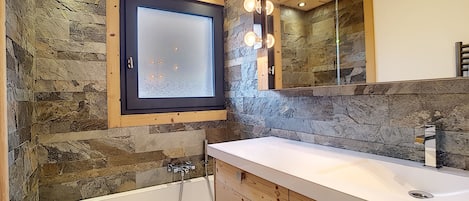 A bathroom with a stone wall, wooden ceiling, a large mirror, and a bathtub.
