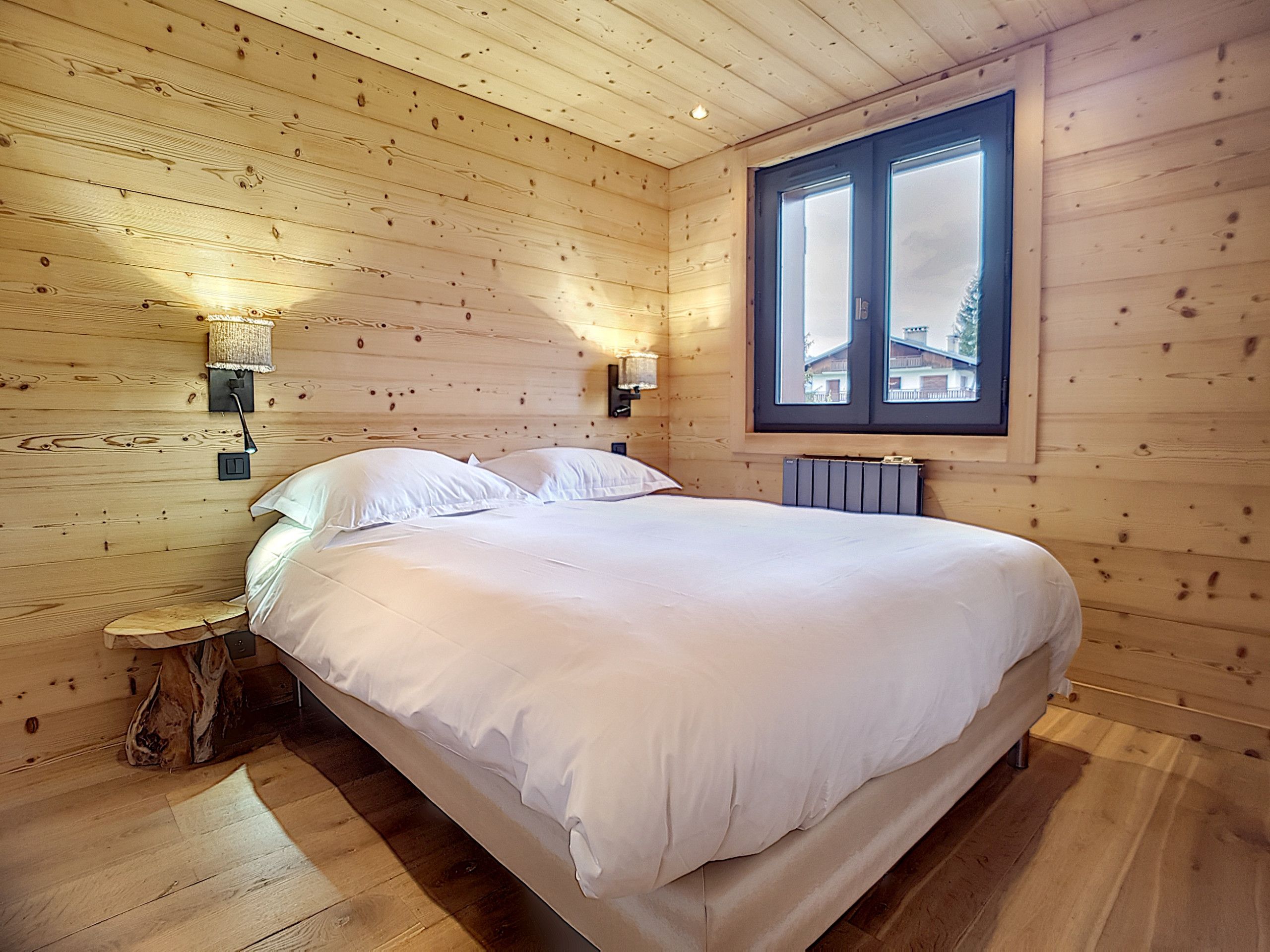 Ein Schlafzimmer mit Holzwänden, einem großen Bett, zwei Nachttischlampen und einem Fenster mit Blick auf Gebäude.
