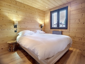 A wooden-paneled bedroom with a large bed, two bedside lamps, and a window with a view of buildings outside.