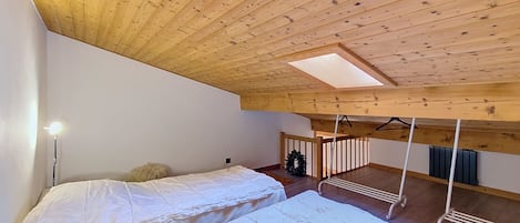 Ein Zimmer mit schrägem Dach, Holzbalken, einem Bett mit weißer Bettwäsche, einer Hängeleuchte und einem kleinen Weihnachtskranz.