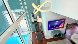 Ein modernes Wohnzimmer mit großem Fernseher, einer Couch, einem Couchtisch und Blick auf einen Swimmingpool.