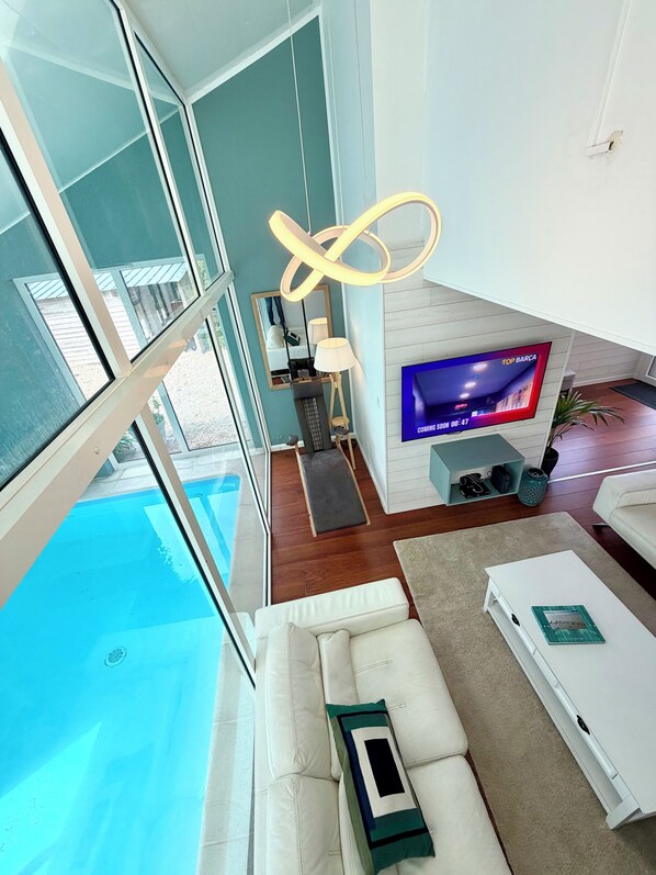 Una sala de estar moderna con un televisor grande, un sofá, una mesa de centro y vistas a una piscina.