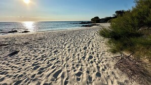 Ein Sandstrand mit Fußabdrücken, einem klaren Himmel und strahlender Sonne.
