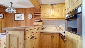 A kitchen with wooden cabinets, a sink, a stove, and a clock on the wall. - 1 RR6183 - (Megève)