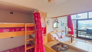A room with bunk beds, a sofa, a table with a painting, a mirror, and a window with a view. - 1 RR6183 - (Megève)