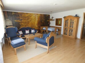 Una sala de estar con un amplio mural con tema de bosque, muebles de madera y un aparador con puertas de vidrio.