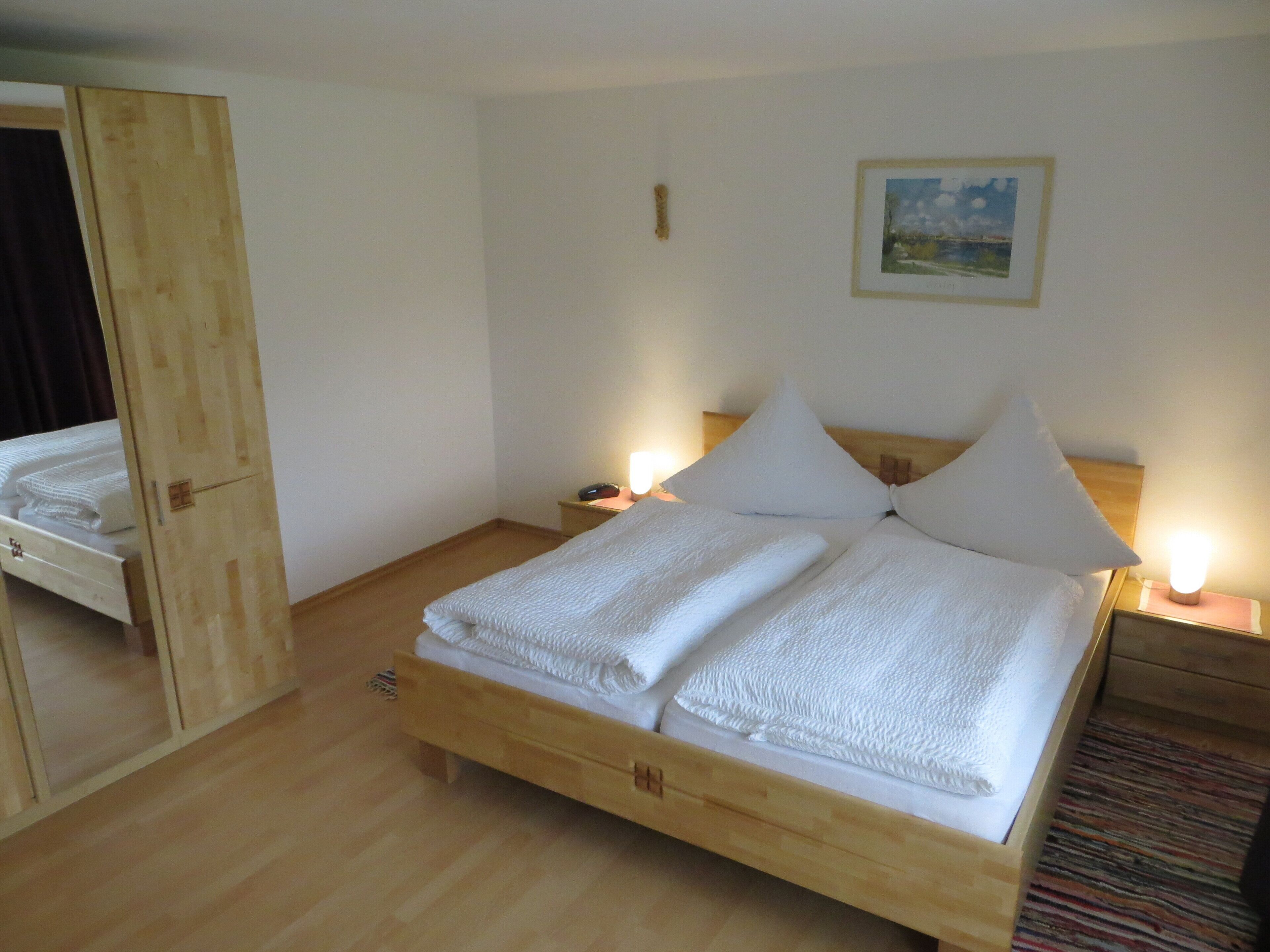 A neatly made bed with white linens, a wooden headboard, and two bedside lamps.