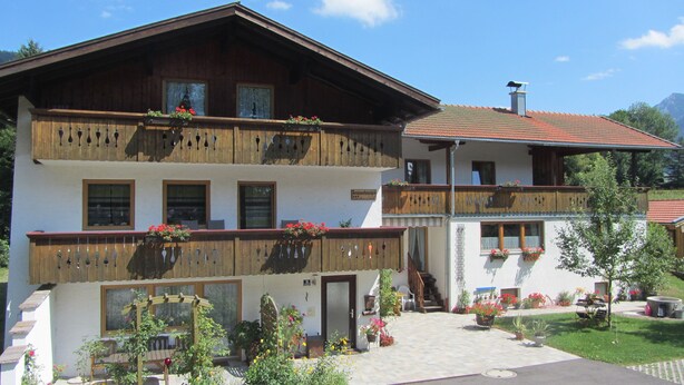 Ein zweistöckiges Gebäude mit hölzernen Balkonen, Blumenkästen und einer gepflasterten Eingangsbereich.