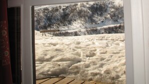A view through a window of a snowy landscape with a wooden deck and a bench. - Les Menuires, charming renovated two-room apartment at the foot of the slopes    (Les Belleville)