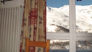 A room with a view of a snowy mountain, a wooden chair, a radiator, and a curtain with a pattern. - Les Menuires, charming renovated two-room apartment at the foot of the slopes    (Les Belleville)