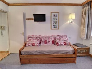Une chambre avec un lit en bois, un téléviseur fixé au mur, un ensemble de photos encadrées, une lampe de chevet et un téléphone mural.