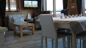 En hyggelig stue med et træbord dækket til spisning, en behagelig sofa og et fjernsyn ophængt på væggen.
