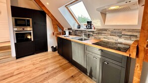 A modern kitchen with a wooden ceiling, built-in appliances, and a stone backsplash. - La Rose des Vents 4 people  (Grandcamp-Maisy)