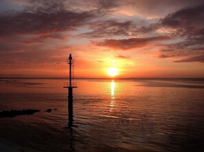 Un faro al atardecer, con el sol reflejado en el agua.