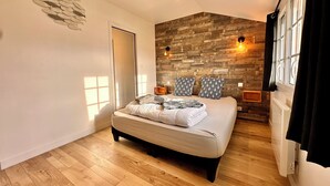 A bedroom with a large bed, wooden wall paneling, two bedside lamps, and a window with curtains. - La Rose des Vents 4 people  (Grandcamp-Maisy)