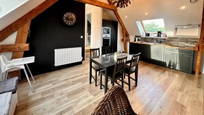 A modern loft with a dining area, kitchen, and a large window. - La Rose des Vents 4 people  (Grandcamp-Maisy)