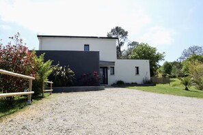Ein modernes, zweistöckiges Gebäude mit einem Schotterweg, der zu einem schwarzen Carport führt.