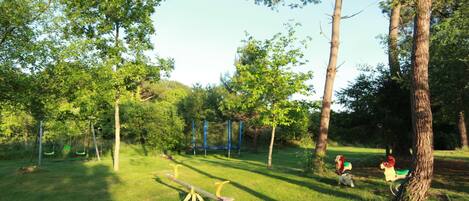Un parc verdoyant avec des arbres, une balançoire et un jeu de bascule.