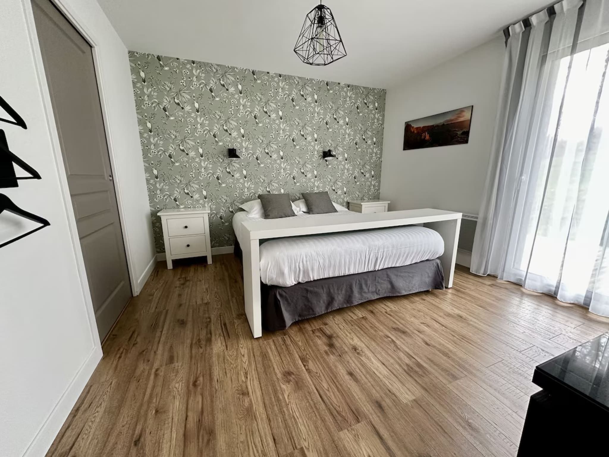 Une chambre à coucher comprenant un lit, des tables de chevet, une commode, une lampe fixée au mur et un tableau.