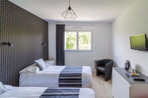 Une chambre d’hôtel avec deux lits, un bureau, une chaise, une télévision et une fenêtre donnant sur des arbres.