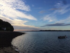 A beach with a calm sea, a boat on the water, and a distant shoreline.