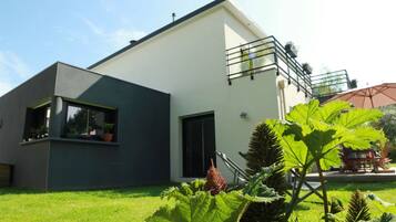 A modern two-story house with a flat roof, a balcony, and a well-maintained lawn.