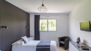 Et hotelværelse med to senge, et skrivebord, en stol, et fjernsyn og et vindue med udsigt til træer.